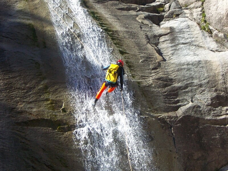 Personne en combinaison rouge descend en rappel le long d'une cascade dans un environnement naturel rocheux.