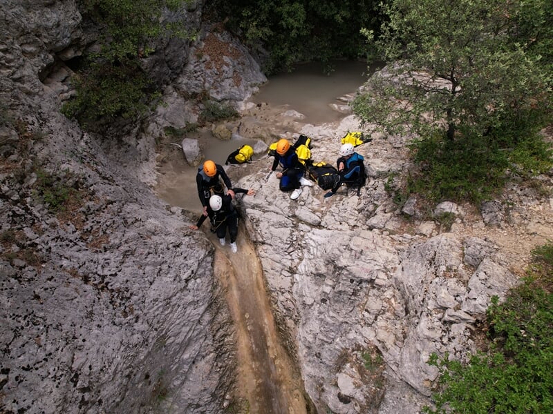 Groupe de personnes en casque et combinaison assis sur des rochers au bord d'une rivière en canyoning.