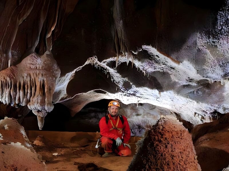 un fomme est accroupi dans la grotte en combinaison de spéléo