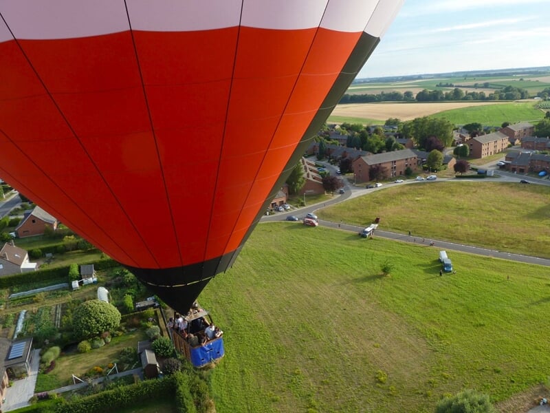 Vue aérienne d'une montgolfière rouge et blanche au-dessus d'un village et de champs verts.