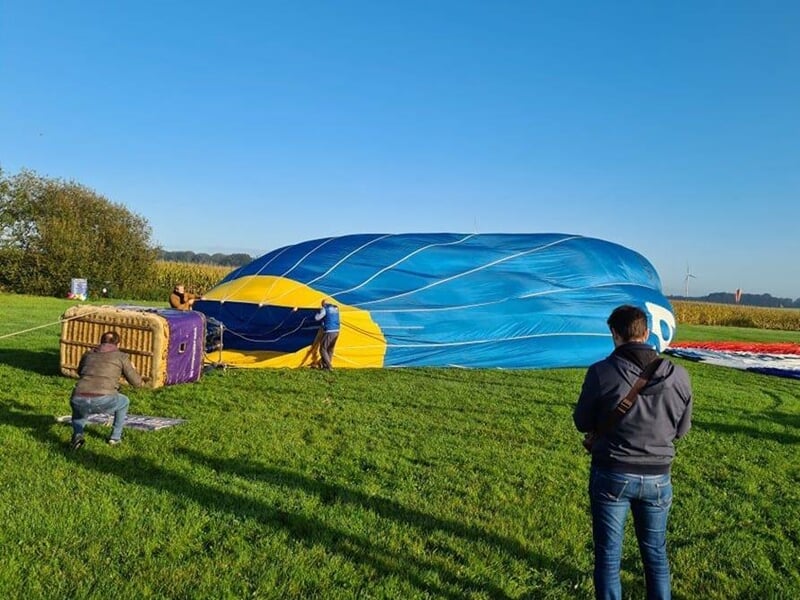 Montgolfière bleue en cours de gonflage sur un champ vert avec plusieurs personnes autour.