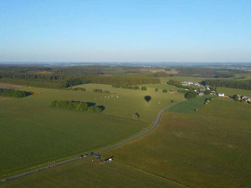 Ombre d'une montgolfière projetée sur un champ vert avec une route et des maisons à proximité.