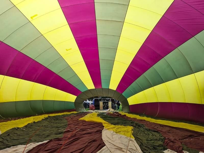 Montgolfière multicolore vue de dessous, flottant dans un ciel clair au-dessus d'un champ vert.