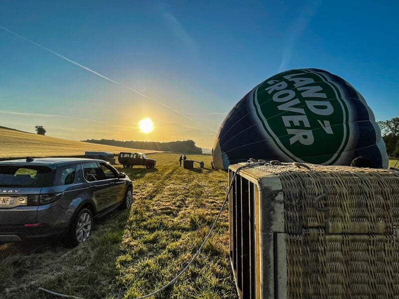Montgolfière Land Rover dégonflée dans un champ avec plusieurs véhicules et le soleil bas à l'horizon.