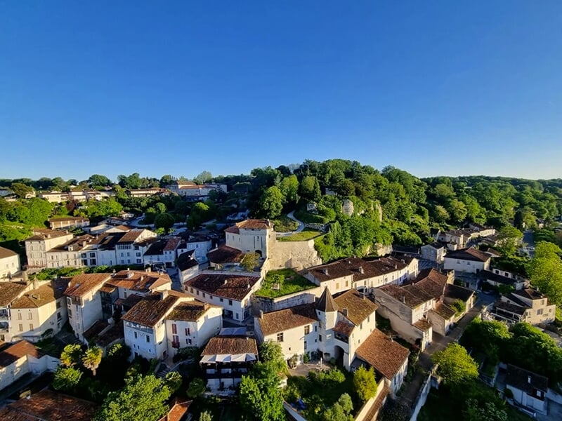 Montgolfière jaune volant au-dessus d'un paysage rural avec champs, forêts et villages sous un ciel clair.