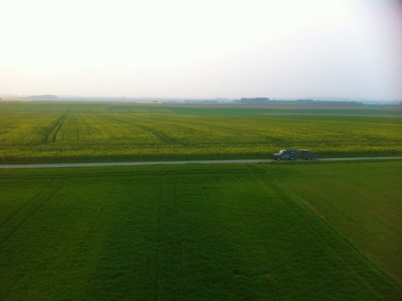 Vue aérienne d'un paysage rural avec champs verts et une route traversant la campagne à l'horizon.