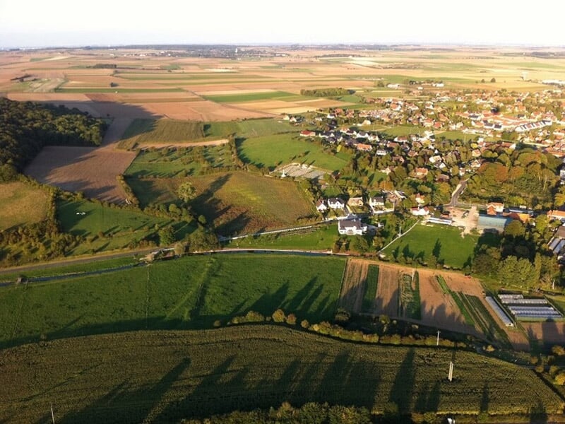 Vue aérienne d'un village entouré de champs cultivés et de routes, prise depuis une montgolfière en vol.