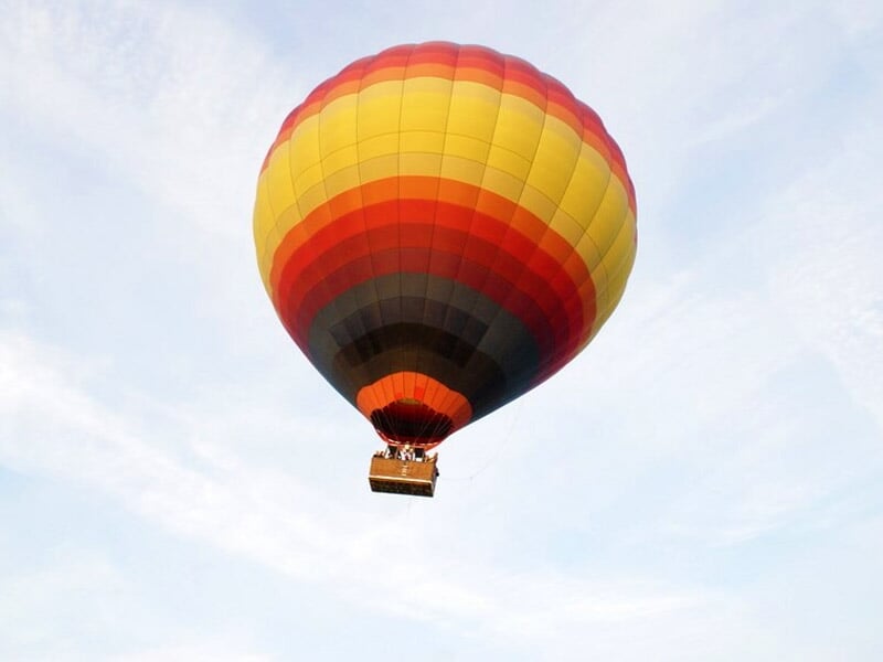 Montgolfière en vol avec une nacelle suspendue, vue de dessous avec un ciel clair en arrière-plan.