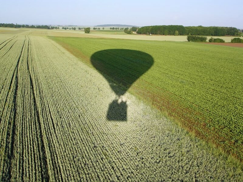 Montgolfière bleue et verte en vol dans un ciel bleu clair, vue de dessous avec la nacelle suspendue.