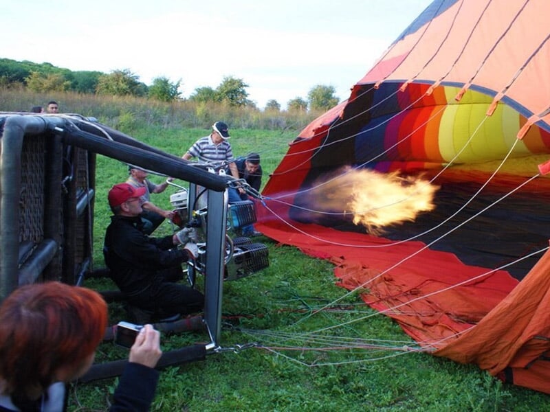 Groupe de passagers souriants dans la nacelle d'une montgolfière en vol, sous un ciel bleu clair.