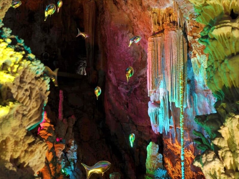 Intérieur d'une grotte avec des stalactites colorées et des poissons lumineux suspendus dans l'air
