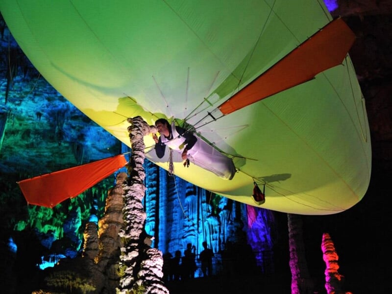 Personne suspendue sous un ballon dirigeable vert dans une grotte aux parois colorées