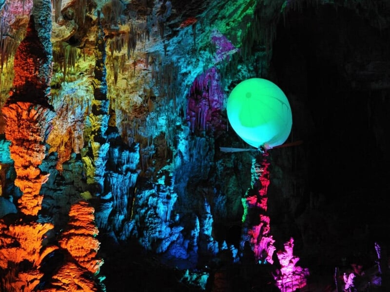 Ballon dirigeable vert suspendu dans une grotte avec des stalactites et des lumières colorées