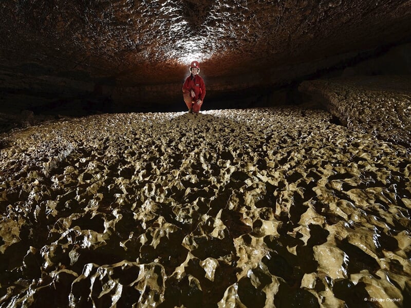 Un spéléologue debout sur une accumulation dense de concrétions calcaires éclairée d'en haut, dans une grotte, créant un contraste de lumière et d'ombre sur la texture pointue du sol