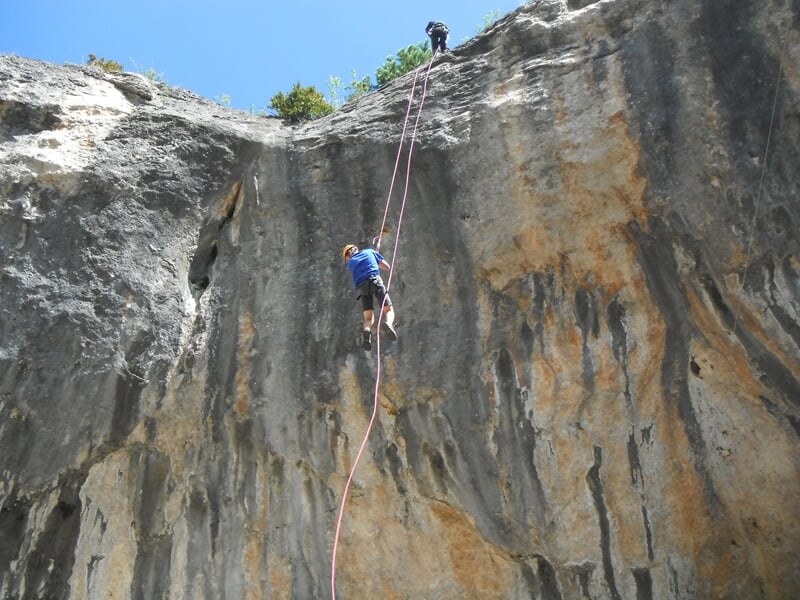 Personne en tenue d'escalade grimpant une falaise abrupte sous un ciel bleu clair en extérieur.