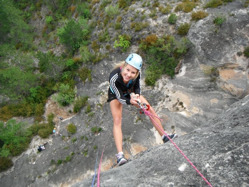 Jeune femme en casque et tenue sportive escaladant une falaise rocheuse avec corde de sécurité rouge.