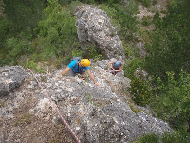 Deux grimpeurs équipés de casques et cordes progressant sur une paroi rocheuse escarpée en nature.
