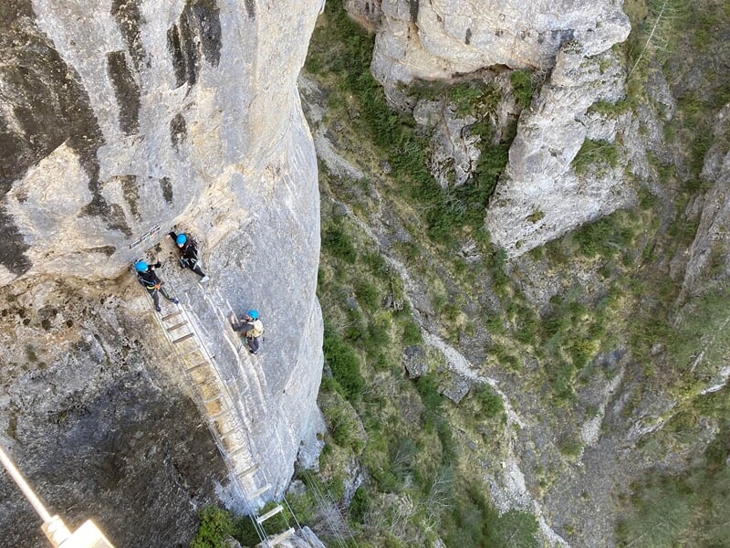 Groupe de personnes en casque traversant un pont suspendu en bois entre deux falaises rocheuses.