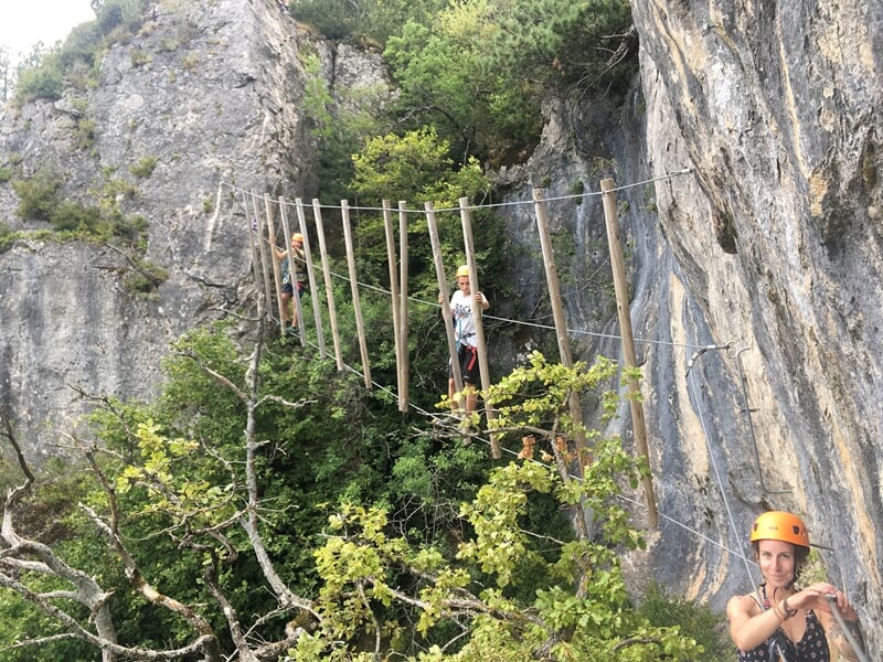 Personnes en casque franchissant un pont de corde étroit entre des falaises dans un cadre naturel.