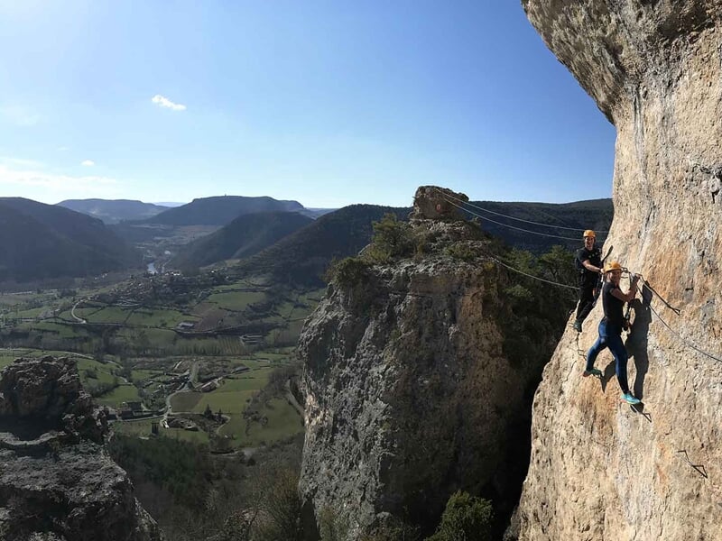 Deux grimpeurs en tenue sportive escaladant une falaise rocheuse avec vue panoramique sur vallée.