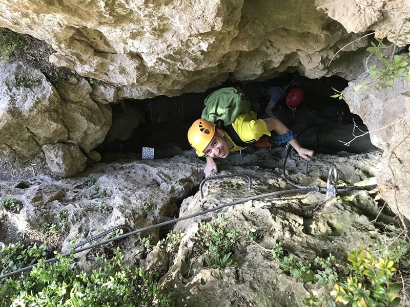 Personnes en casque progressant dans une grotte rocheuse étroite équipée pour via ferrata aventure.