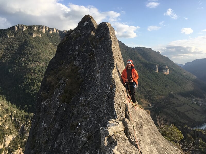 Personne en casque et équipement d'escalade sur une arête rocheuse étroite avec paysage montagneux.
