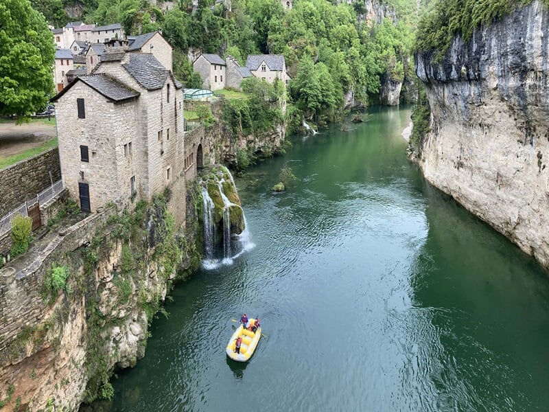 Petit bateau jaune naviguant sur une rivière calme entourée de falaises et végétation dense.