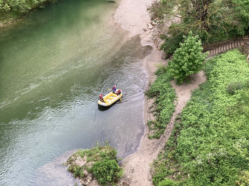 Vue aérienne d'un bateau jaune sur une rivière sinueuse bordée d'arbres et de rochers verts.