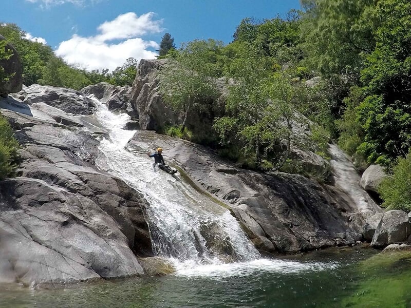 Personne en combinaison de canyoning glissant sur une cascade rocheuse dans un environnement naturel.