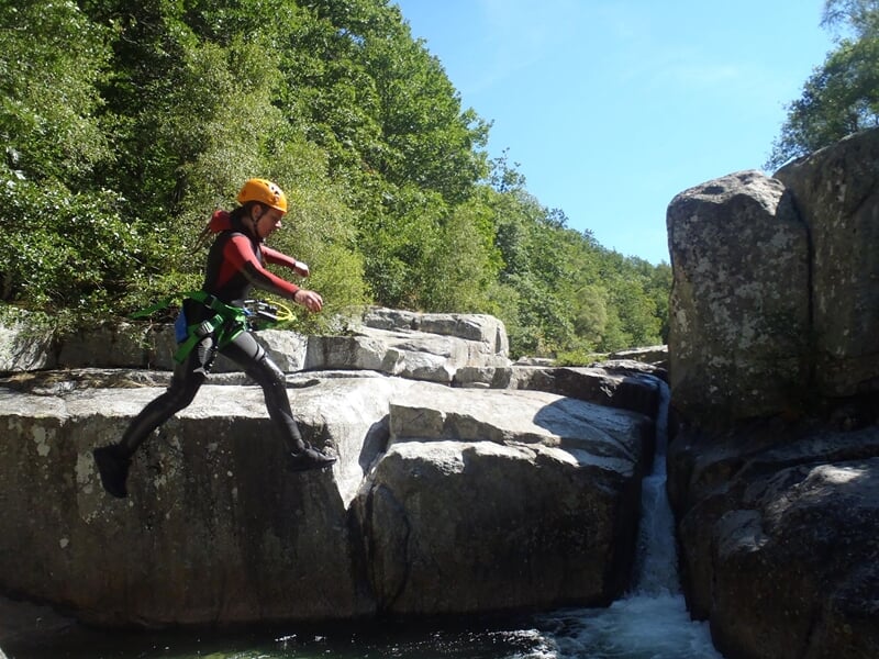 Canyoning dans un cours d'eau rocheux avec cascade, entouré de végétation et rochers naturels.