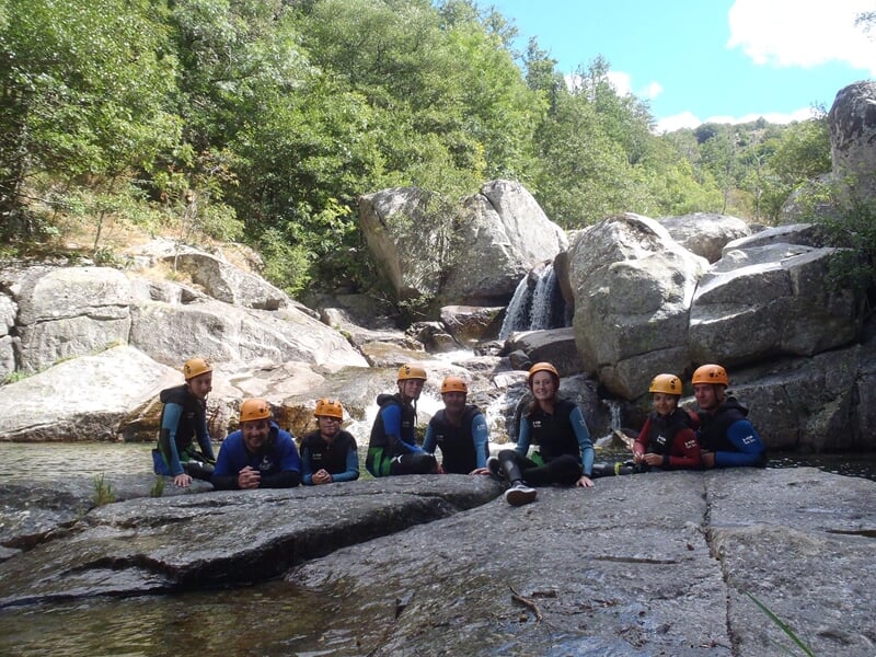 Personne en combinaison de canyoning sautant dans une piscine naturelle formée par une cascade.