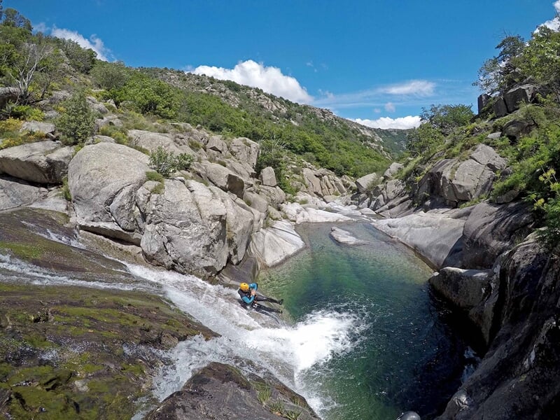 Groupe de canyoning posant sur des rochers au bord d'une rivière dans un cadre naturel verdoyant.
