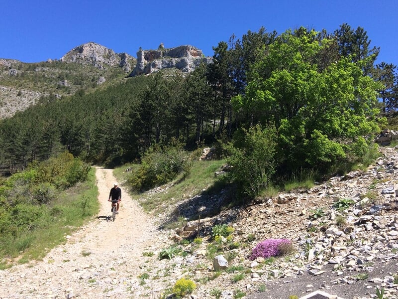 VTTiste pédalant sur un sentier de montagne avec vue sur des collines boisées et ciel bleu.