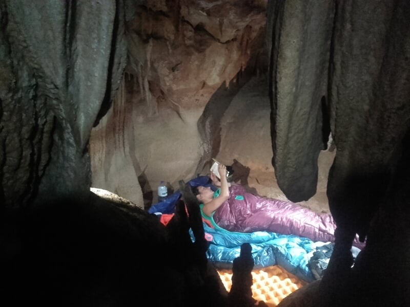 Personne allongée dans une grotte sur un matelas, entourée de stalactites et stalagmites.