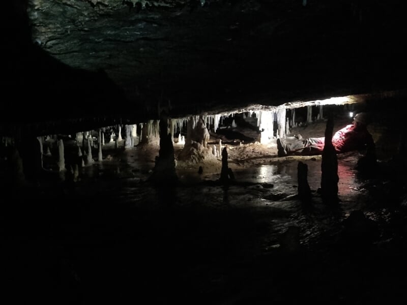 Intérieur sombre d'une grotte avec formations rocheuses et stalagmites éclairées par une lampe.