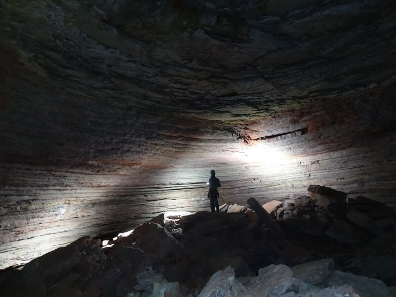 Personne seule dans une grande salle souterraine éclairée par une lampe, entourée de roches.