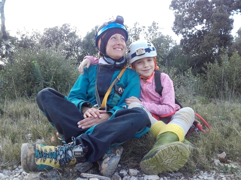 Femme et enfant assis sur un rocher en pleine nature, souriants et équipés de casques de spéléologie.