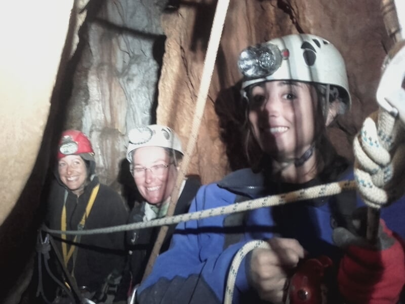 Groupe de spéléologues progressant dans une grotte étroite, équipés de casques et harnais.
