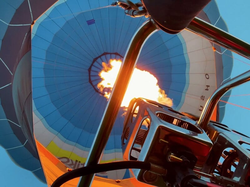 Vue en contre-plongée d'une montgolfière bleue avec la flamme du brûleur en action dans le ciel clair.
