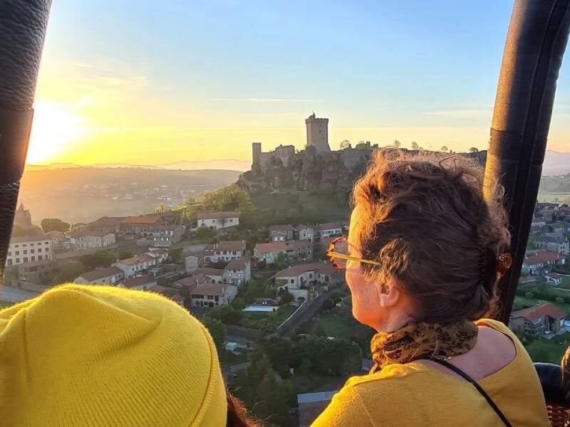 Personnes dans une montgolfière regardant un château médiéval au coucher du soleil au Puy-en-Velay.