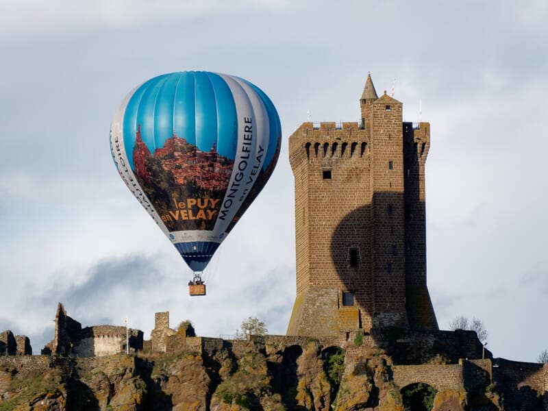 Montgolfière bleue avec inscription Le Puy en Velay près d'un château médiéval lors d'un vol en montgolfière près de Langogne.