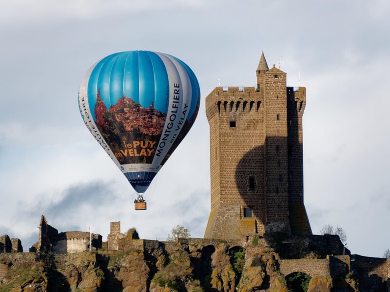Montgolfière bleue avec inscription Le Puy en Velay près d'un château médiéval lors d'un vol en montgolfière près de Langogne.