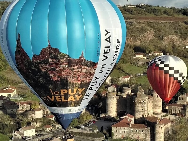 Deux montgolfières colorées volant au-dessus d'un village ancien lors d'un vol en montgolfière près de Langogne.