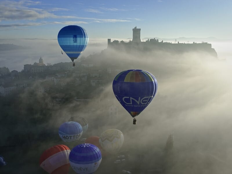 Plusieurs montgolfières colorées flottant dans un ciel brumeux lors d'un vol en montgolfière près de Langogne.