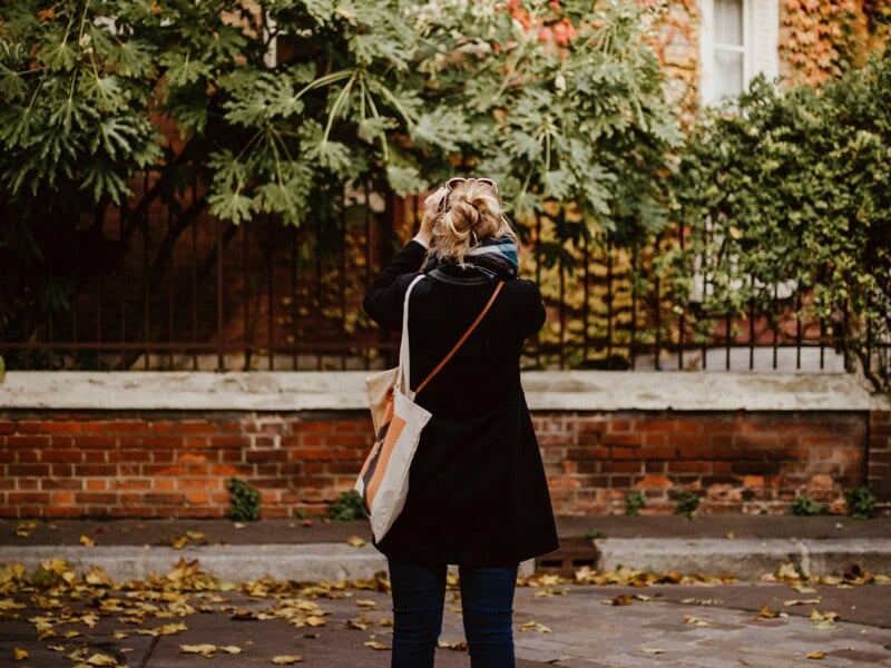 Personne de dos prenant une photo devant un mur de briques couvert de feuilles d'automne à Paris.