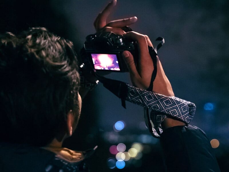 Gros plan sur une main tenant un appareil photo numérique en train de prendre une photo de nuit.