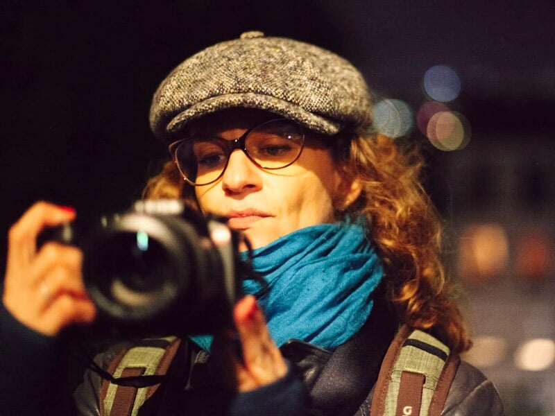 Portrait d'une femme avec casquette et écharpe bleue regardant l'écran de son appareil photo la nuit.