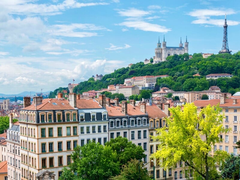Panorama urbain de Lyon avec collines, bâtiments anciens et ciel bleu clair en arrière-plan.