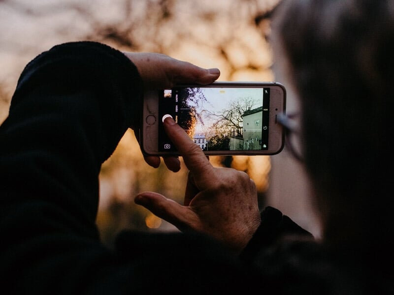 Personne prenant une photo avec un smartphone au coucher du soleil, paysage urbain en arrière-plan.