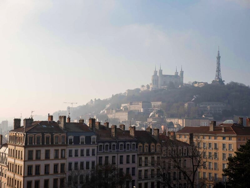 Vue panoramique de Lyon avec collines, bâtiments historiques et ciel clair en fin de journée.